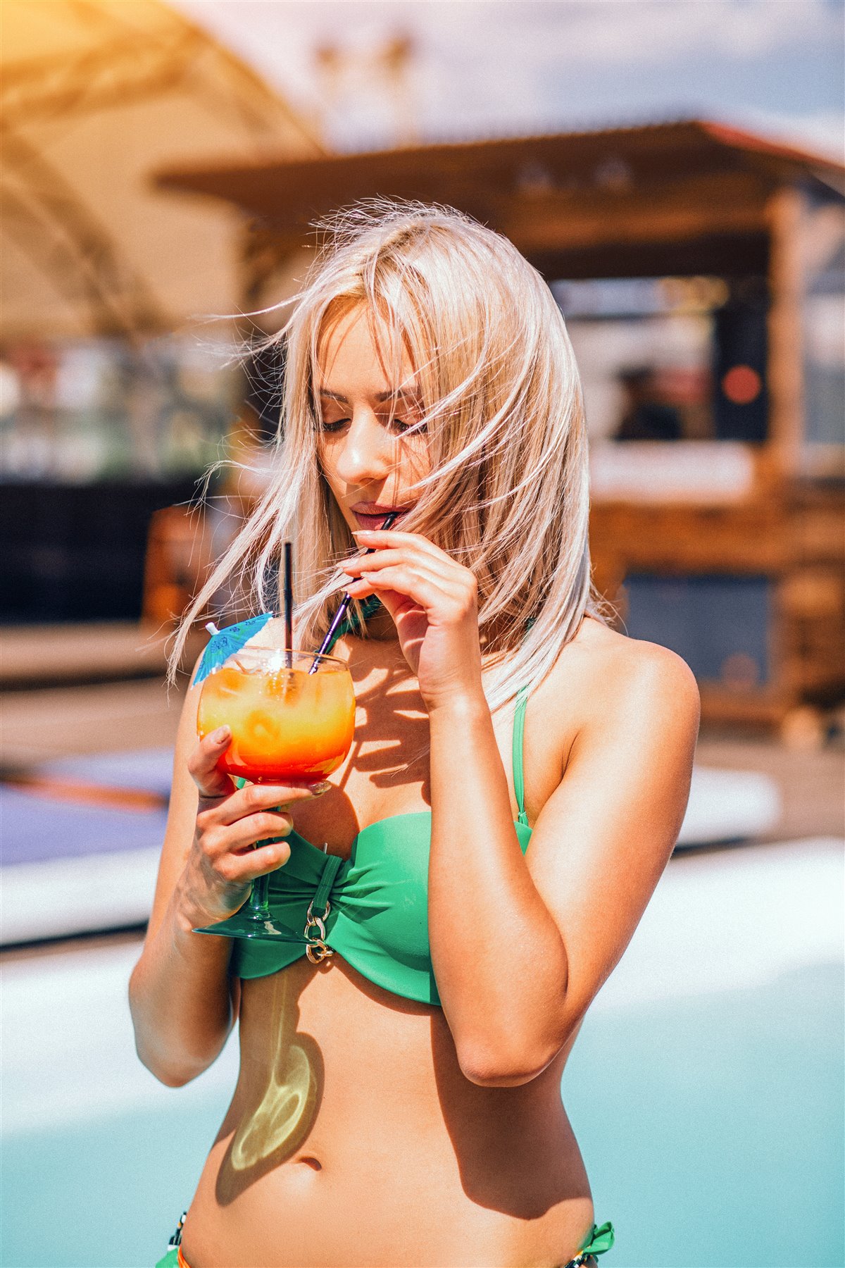 Woman in a green bikini enjoying a bright cocktail by the pool