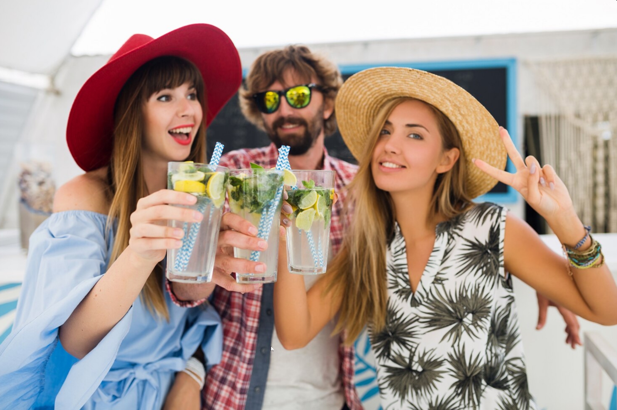 Friends in straw hats raising bright citrus drinks on a sunny patio