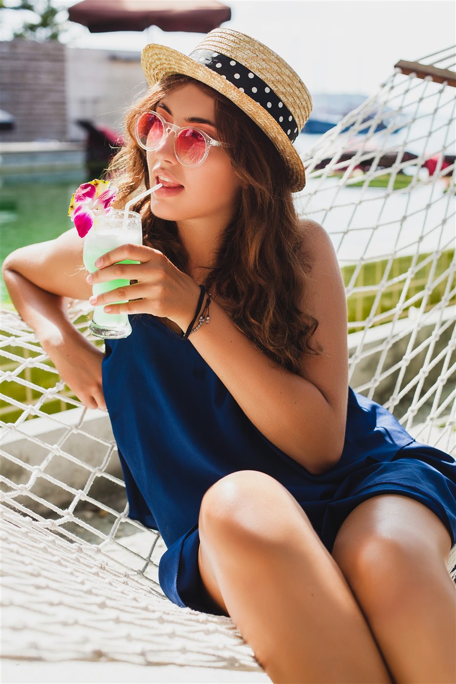 Woman in a straw hat relaxing in a hammock with a tropical cocktail
